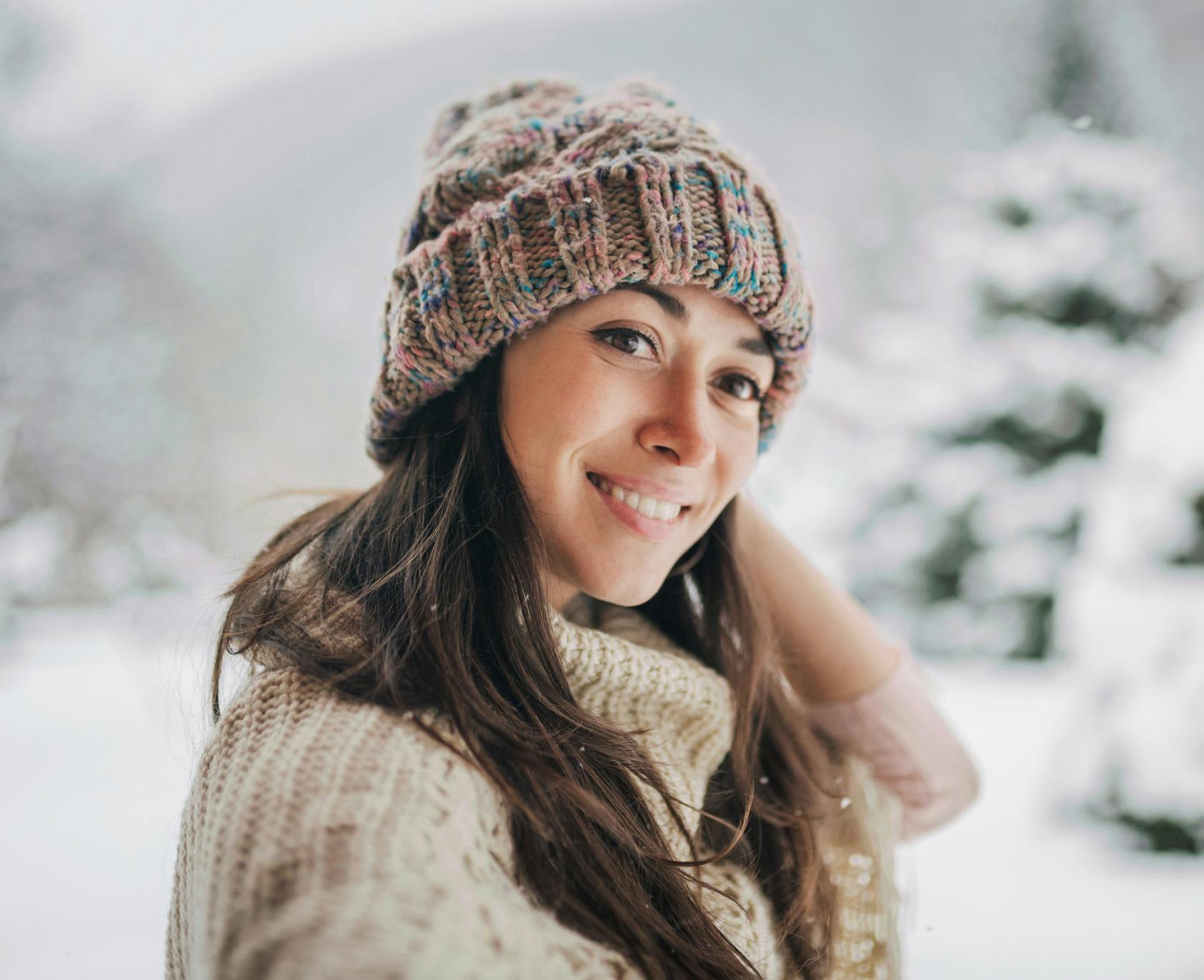 woman in a knitted hat and scarf smiling in the snow