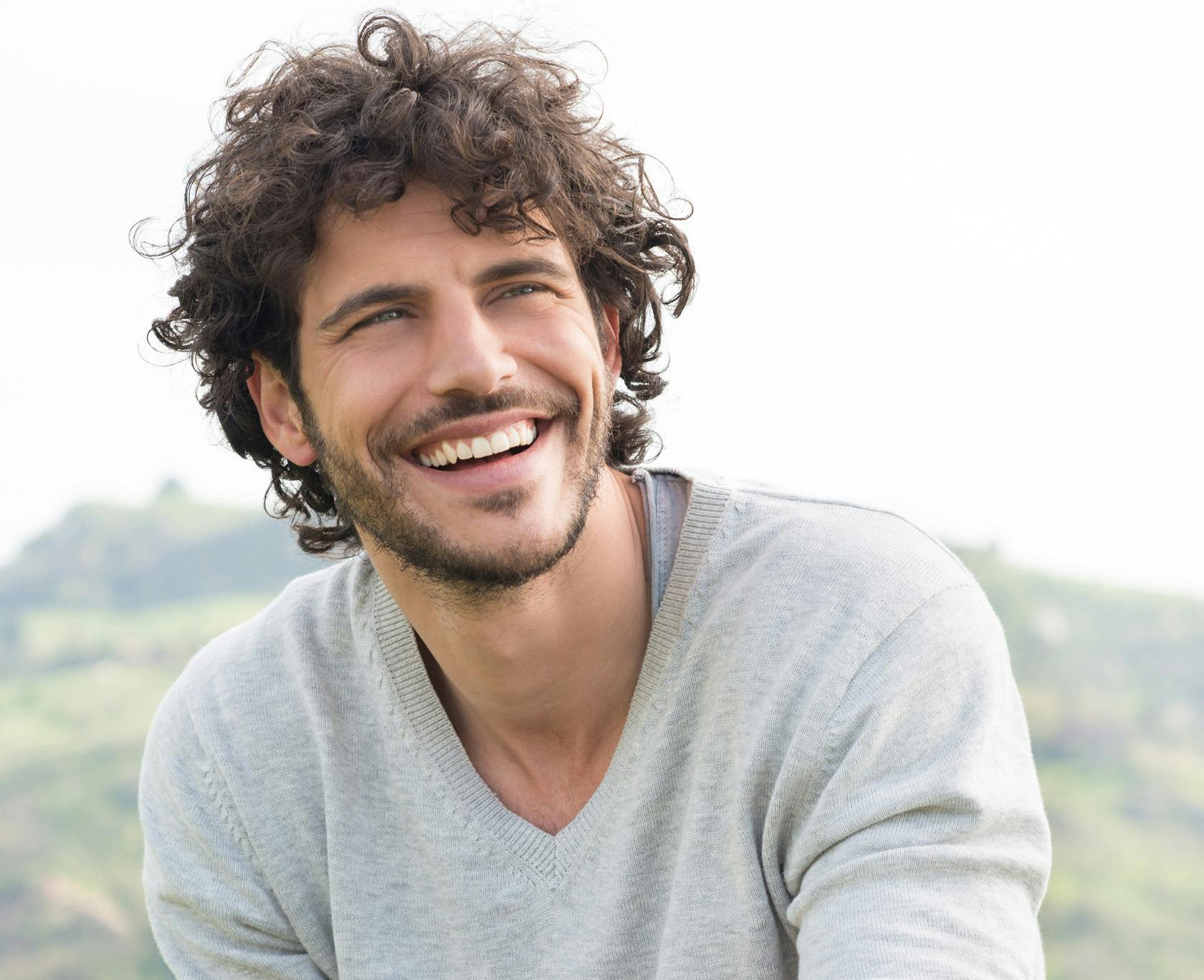 smiling man with curly hair and beard sitting on a hill