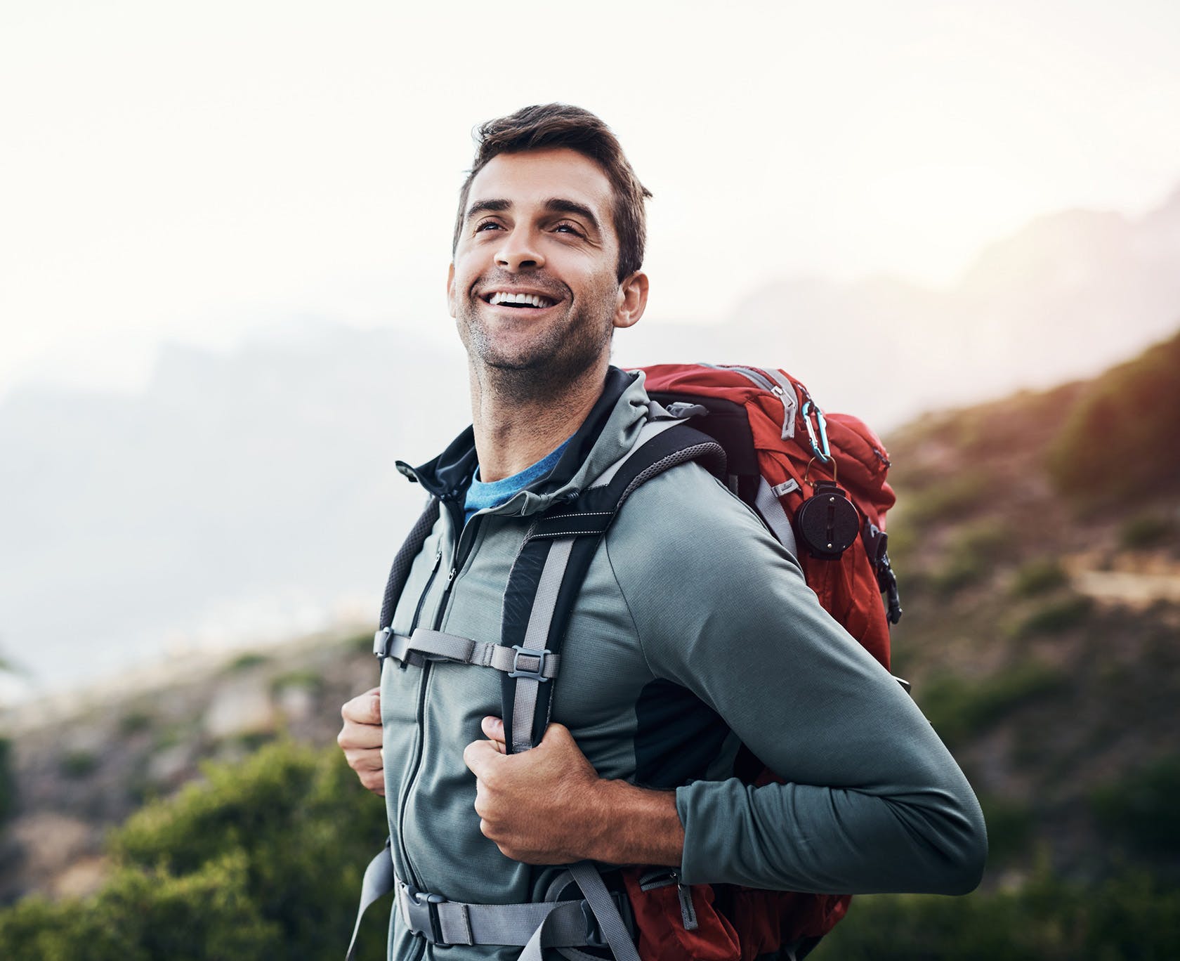 smiling man with backpack on mountain top with mountains in background