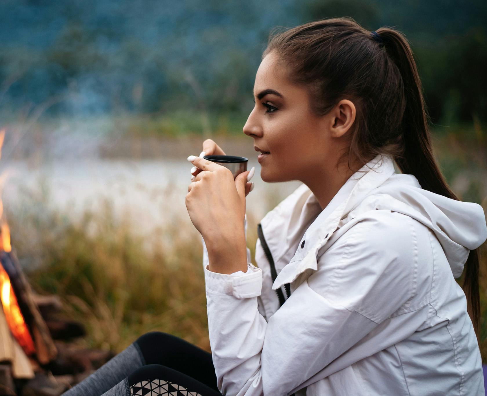 there is a woman sitting by a fire with a cup