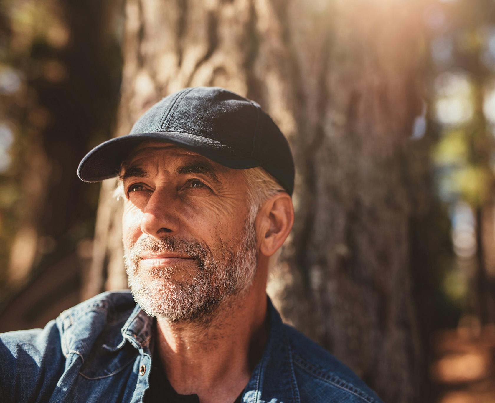 man in a cap and denim shirt sitting in front of a tree
