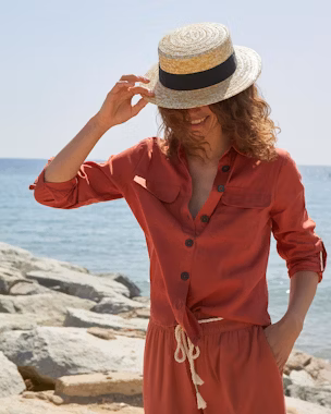 Donna in spiaggia con tuta arancione e cappello di paglia – Moda estate 2025