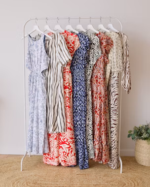 Clothes rail with lightweight summer dresses hanging, featuring trendy floral, stripe and animal prints in white-blue and white-red.