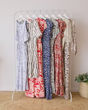 Clothes rail with lightweight summer dresses hanging, featuring trendy floral, stripe and animal prints in white-blue and white-red.