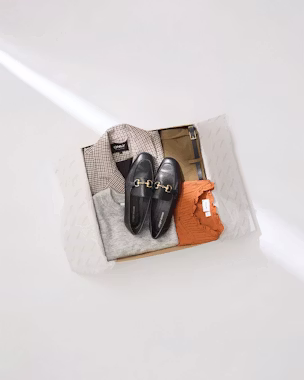 Lookiero box with black women’s loafers, checked blazer, grey jumper and orange blouse, showing how to wear women’s loafers in elegant and versatile everyday outfits.