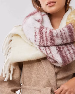 Woman in beige coat with oversized wool scarf in burgundy and white stripes, showing how to tie a scarf with style in winter.