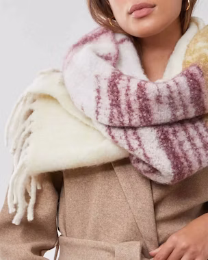 Woman in beige coat with oversized wool scarf in burgundy and white stripes, showing how to tie a scarf with style in winter.