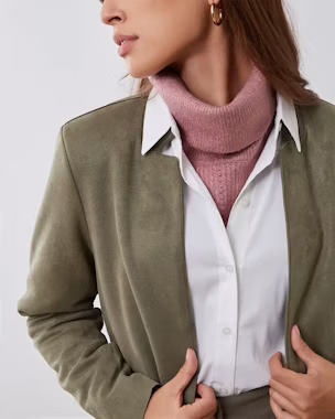 Woman wearing a pink turtleneck under a white shirt and khaki jacket, showcasing a chic and modern women’s layering fashion look.