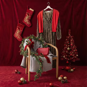 Abito fantasia su una gruccia, maglione rosso, cappotto di lana grigio e borsa rossa su una sedia, decorato in stile natalizio e con sfondo rosso