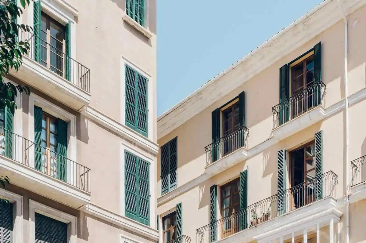Façade d'un immeuble ancien rénové avec balcons en fer forgé et volets verts, illustrant un investissement locatif réussi en déficit foncier.