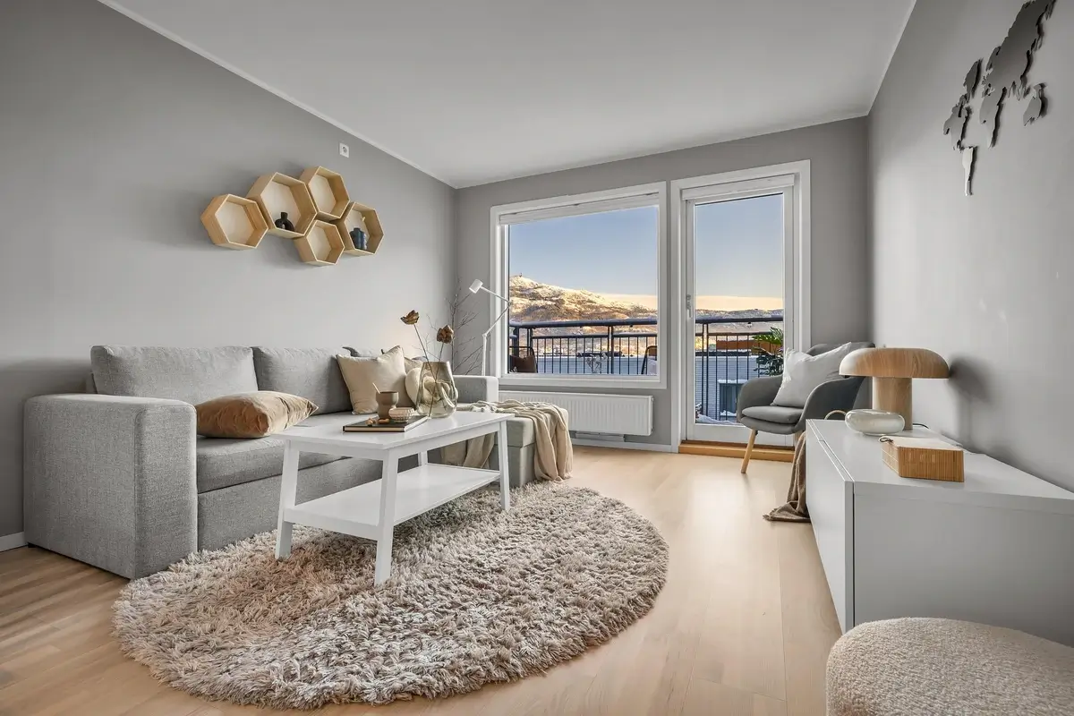 Salon meublé moderne et chaleureux avec canapé gris, tapis rond et grande baie vitrée, parfait pour générer des revenus locatifs via le statut LMNP ou LMP.