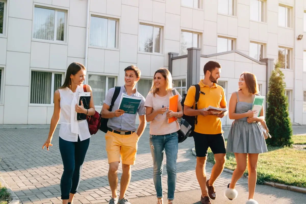 Groupe de cinq étudiants souriants marchant ensemble sur un campus devant leur résidence, illustrant le marché cible d'un investissement en LMNP géré.