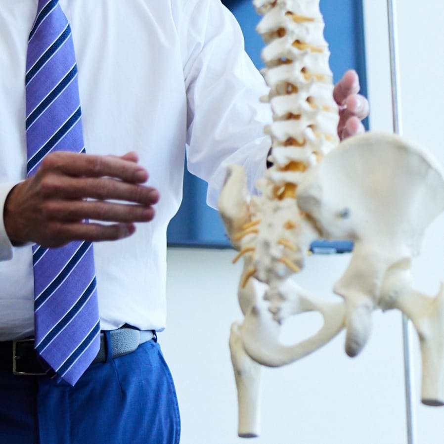 man in a white shirt and blue tie holding a model of a human skeleton