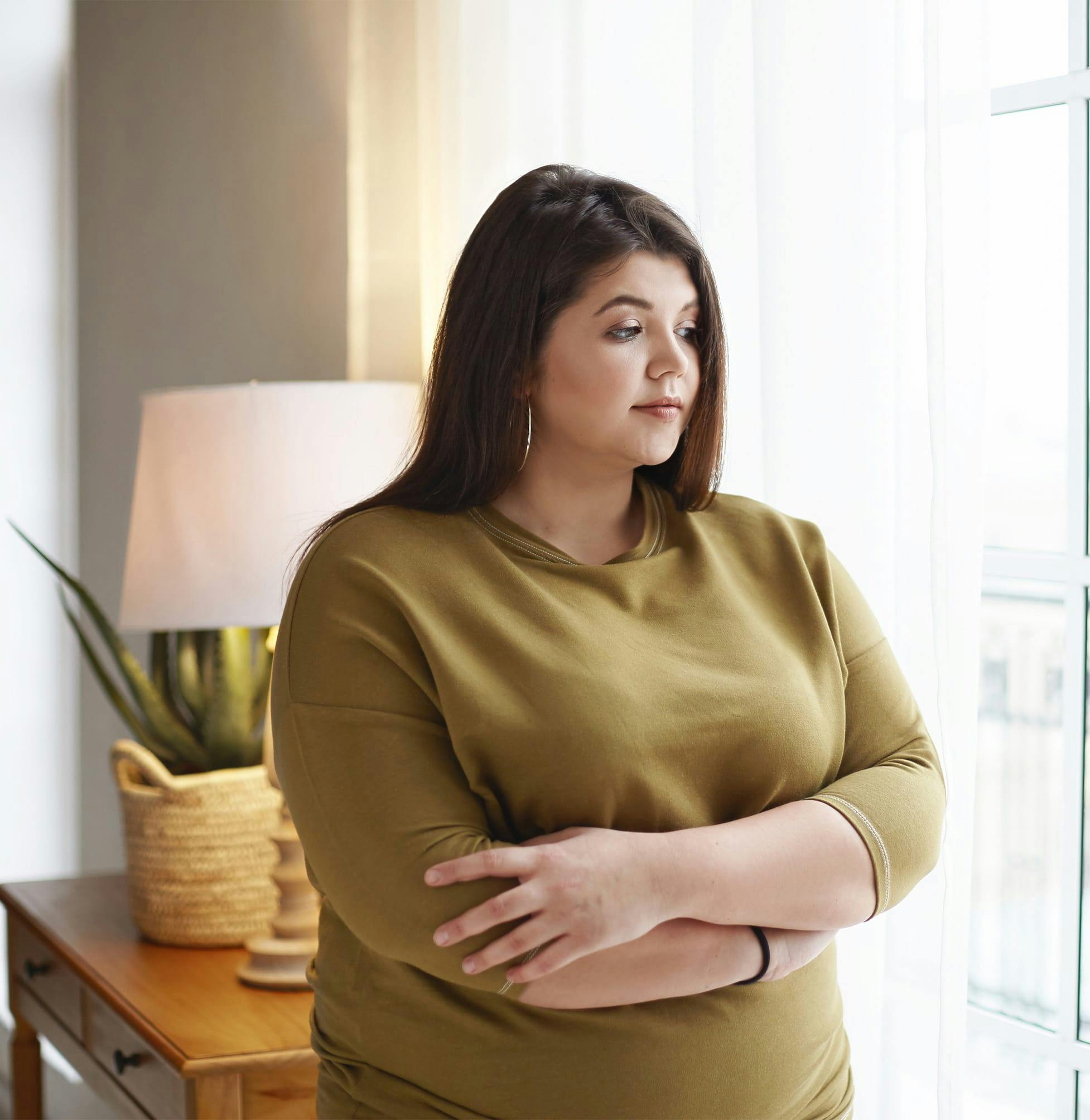 there is a woman standing by a window with her arms crossed