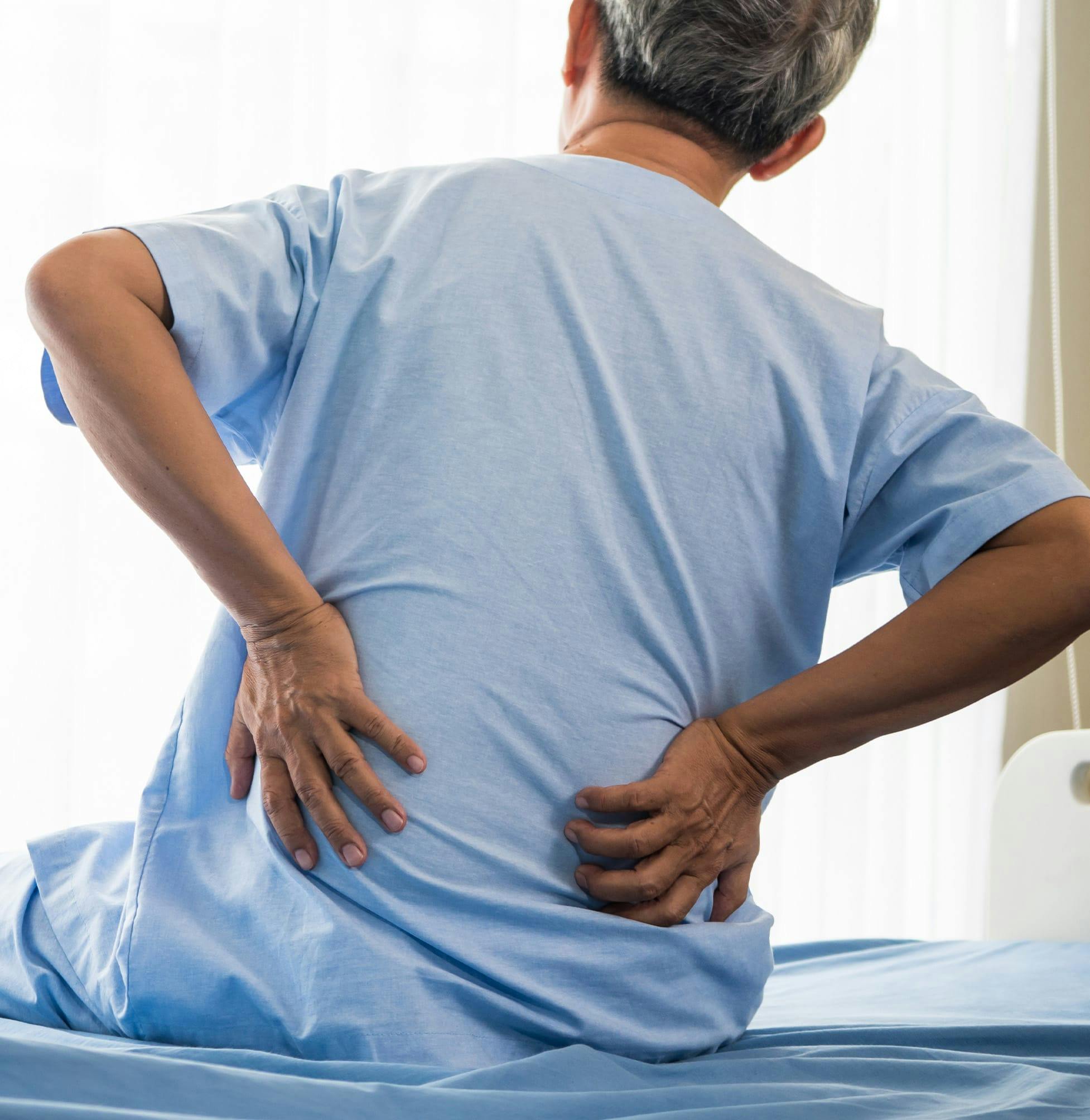there is a man with a back pain sitting on a bed