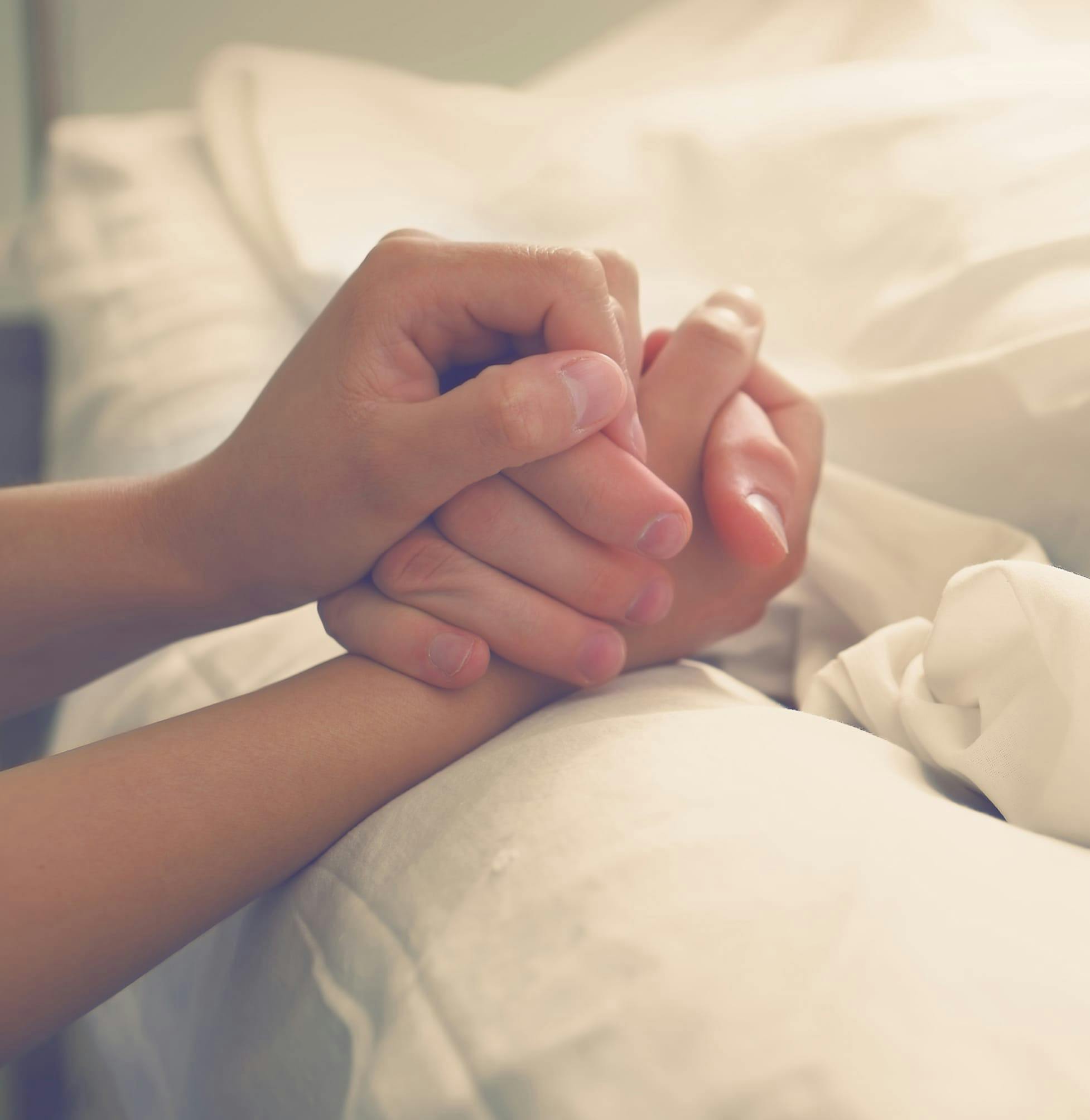 Two people holding hands, one is in a hospital bed.