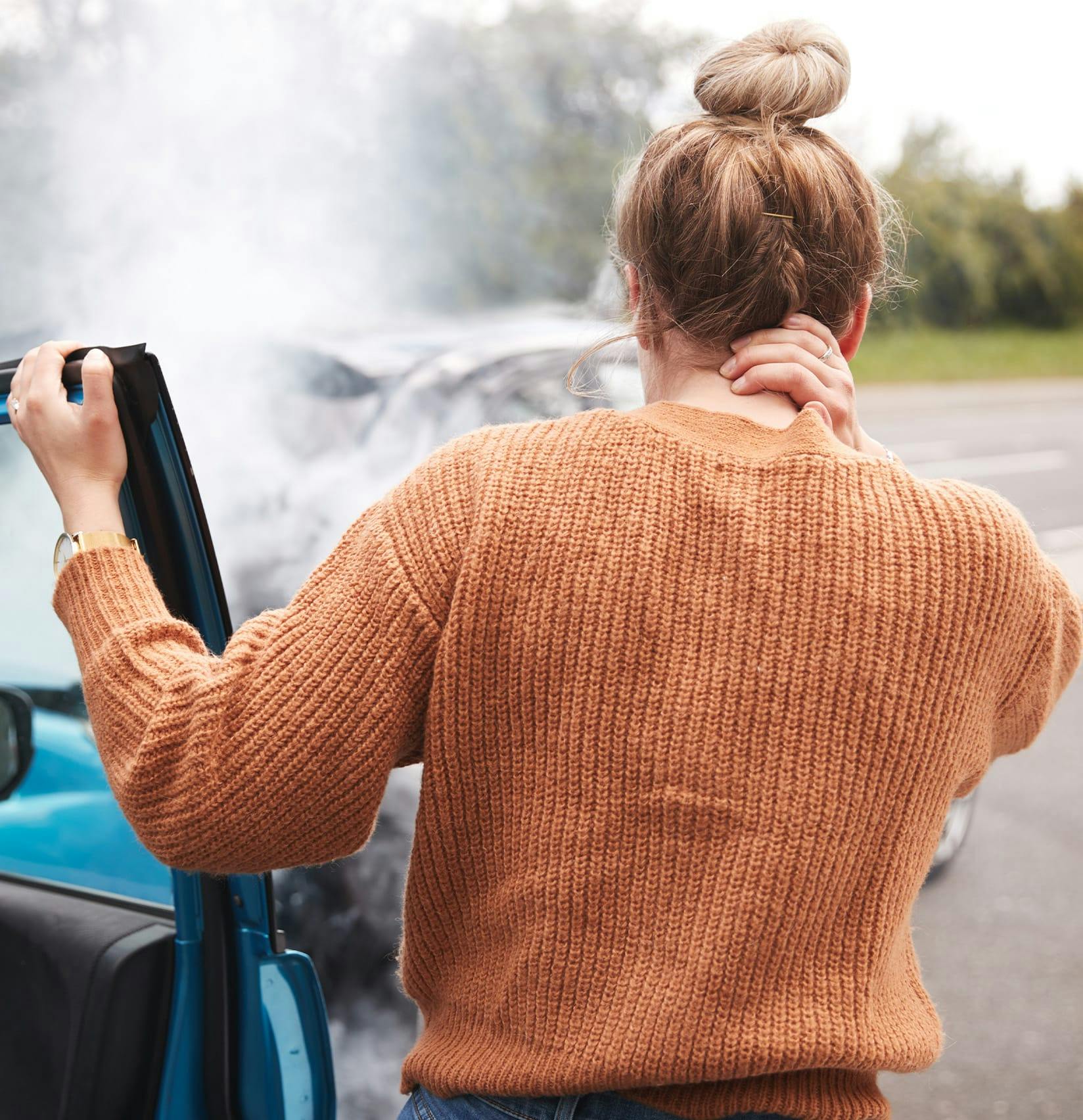 Woman standing next to a car crash holding her neck.