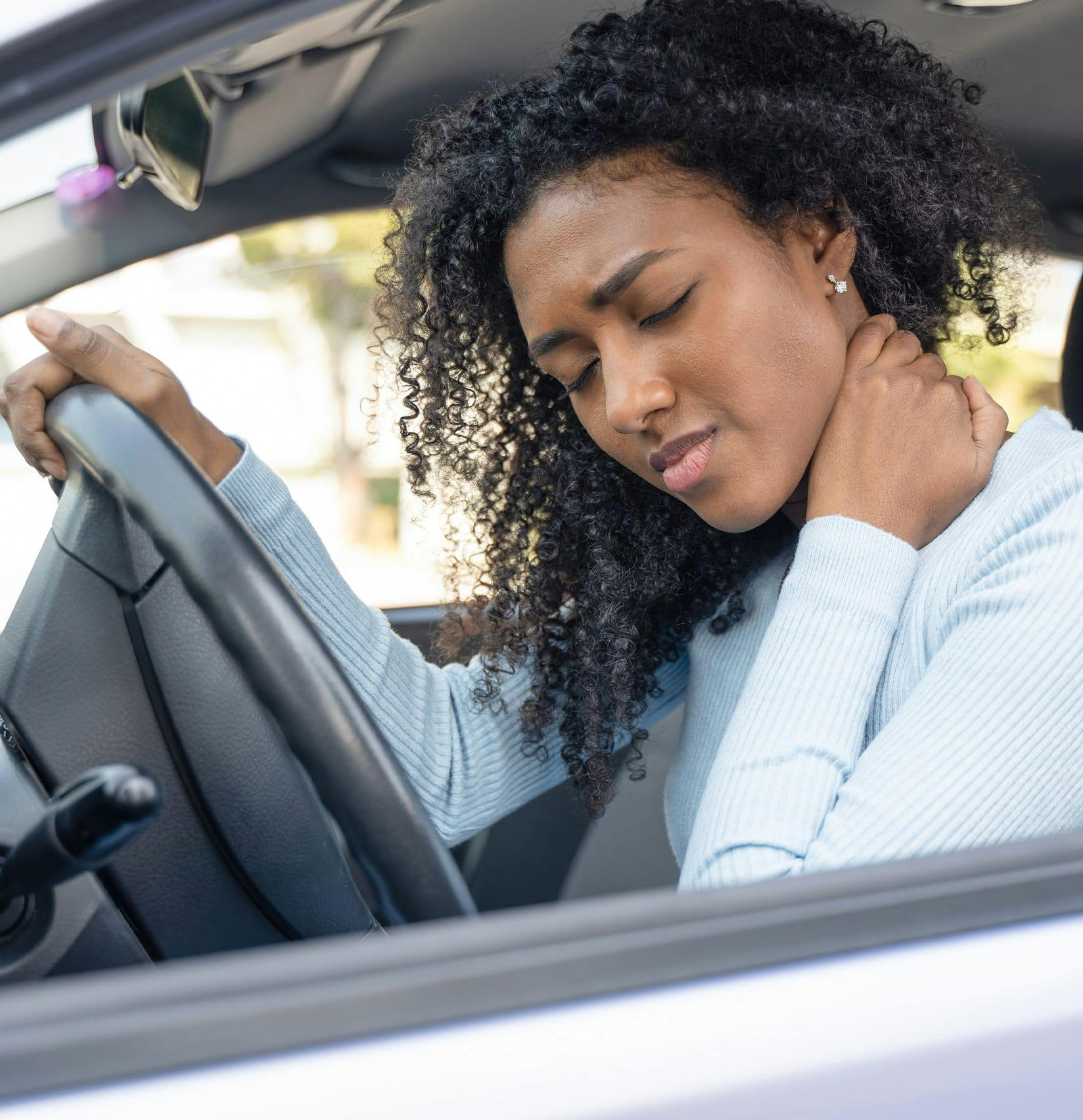 Woman in a car holding her neck in pain