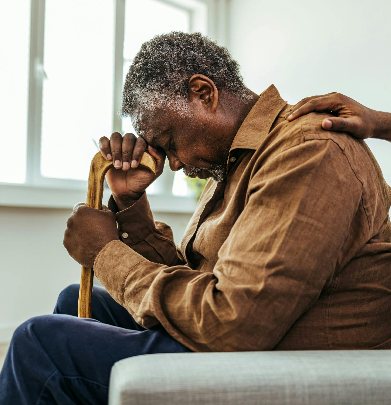 Sad elderly man with his head on his cane