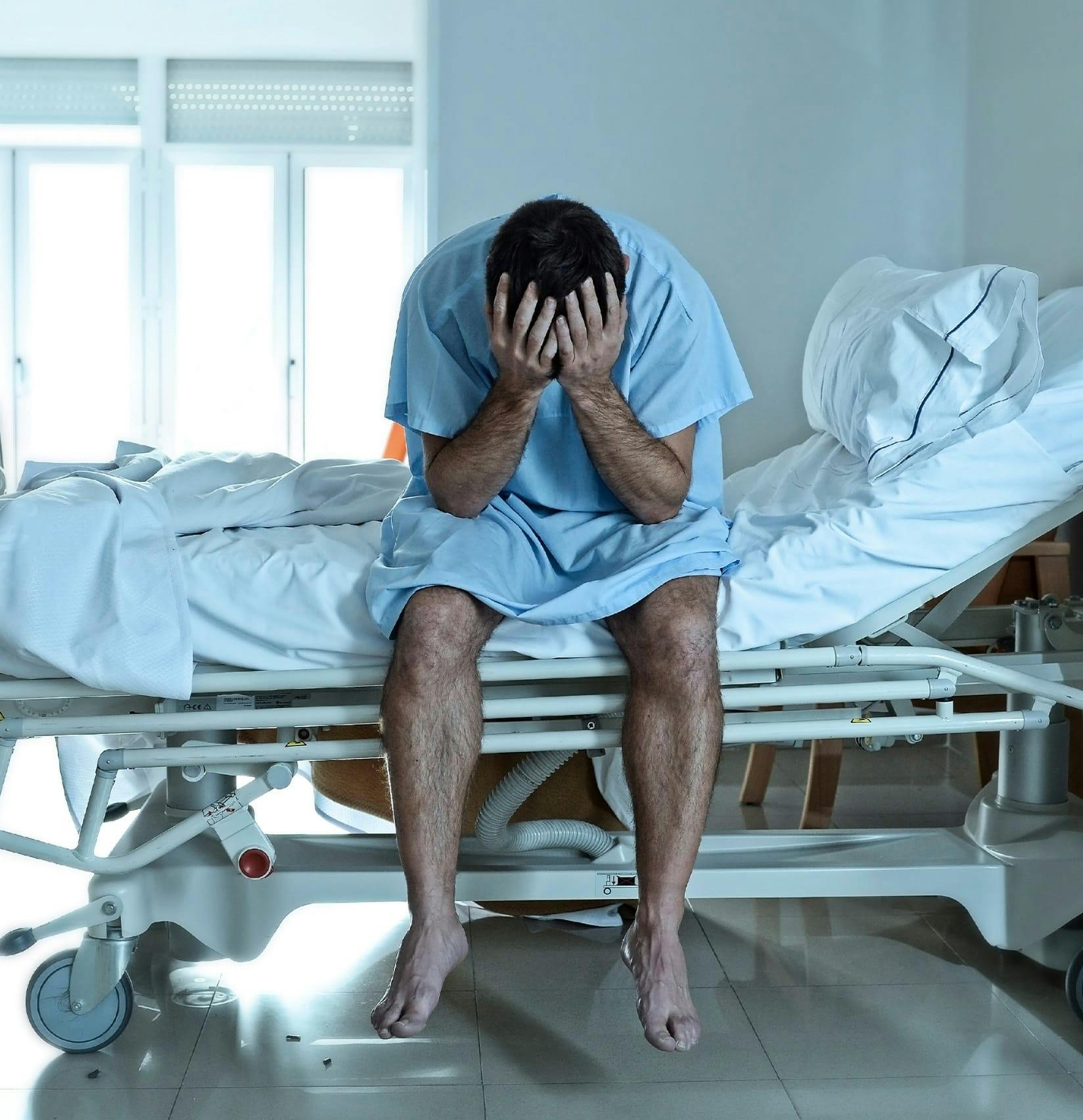 Man holding his head sitting in a hospital bed