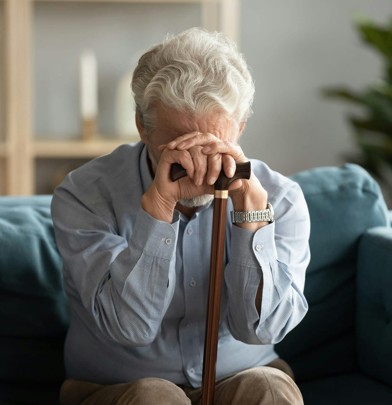 Elderly gentleman with his head bent over his cane.