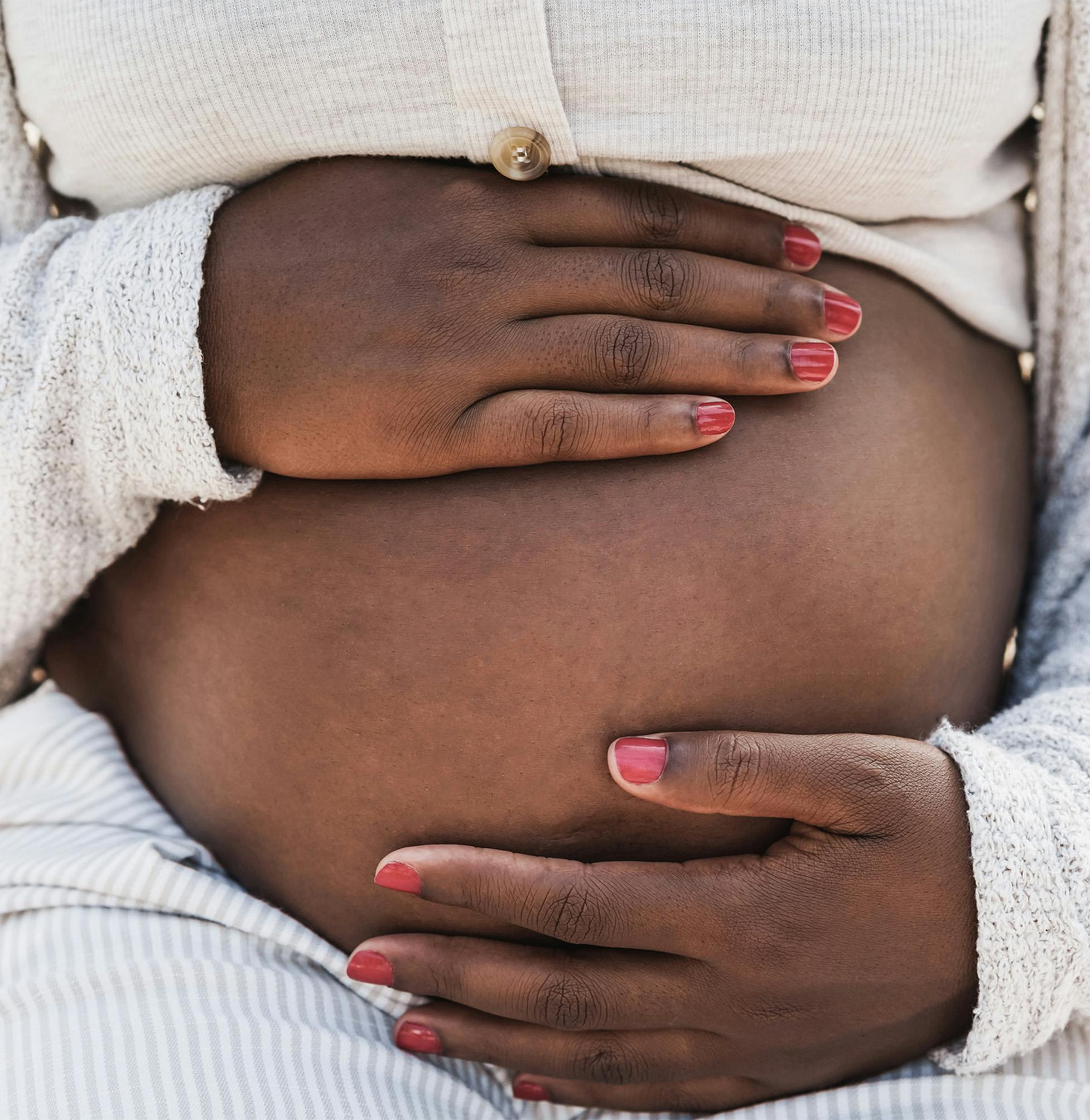 pregnant woman with pink nails and a white sweater holding her belly