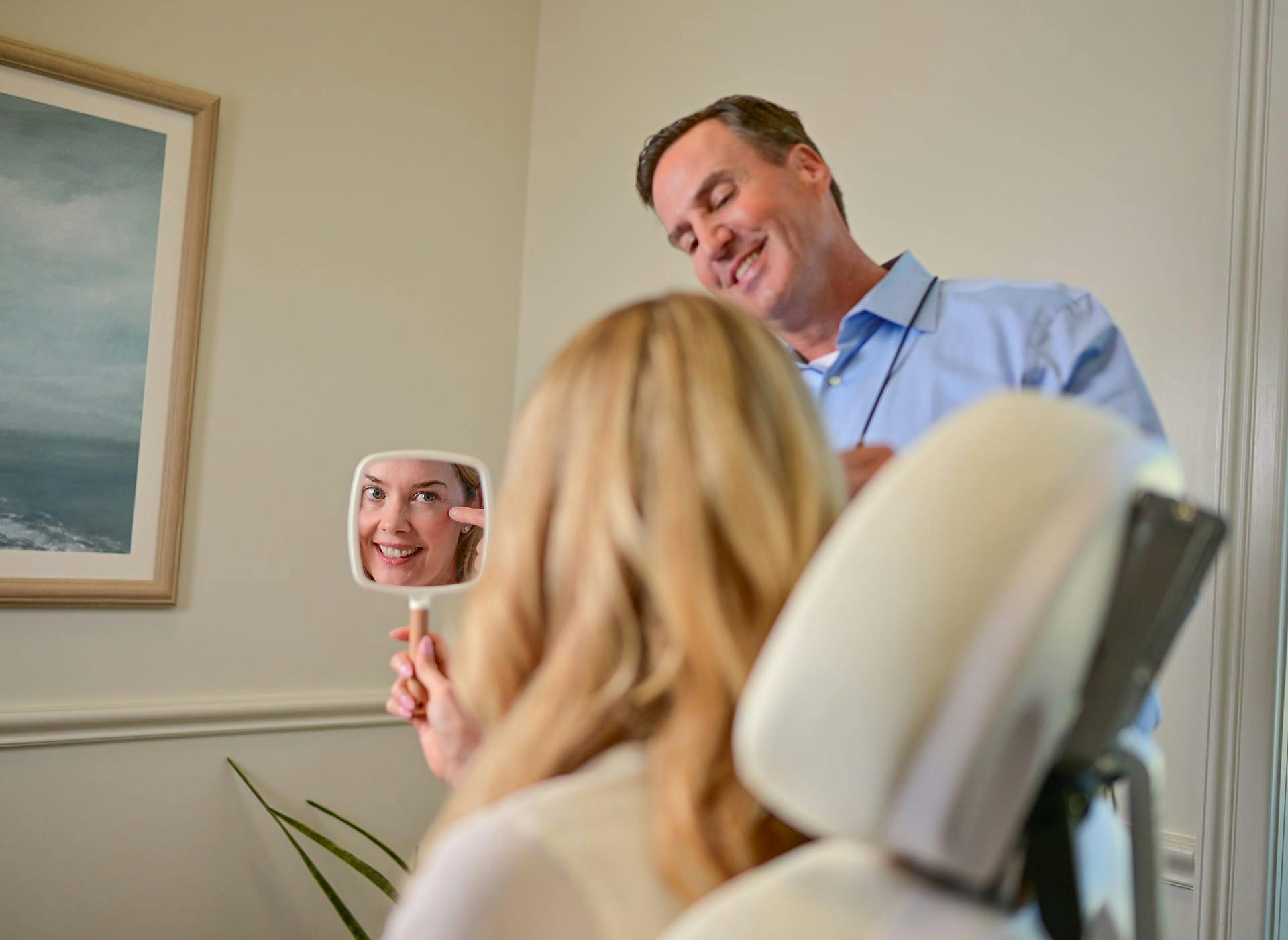 doctor showing patient her facial results on a handheld mirror