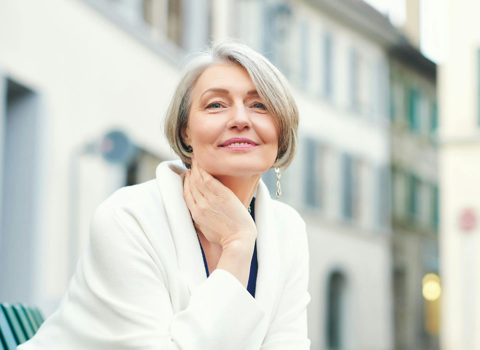 older woman sitting outside with her hand on her neck smiling