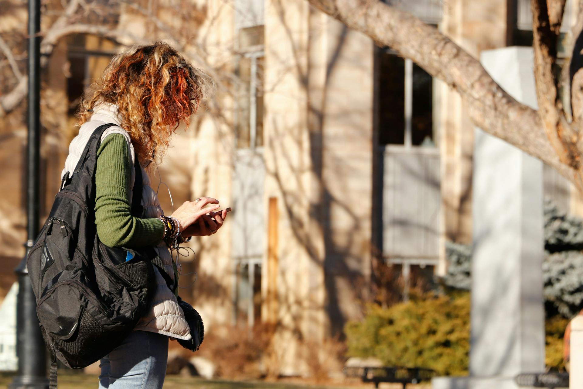Studentin mit Rucksack schaut auf dem Campus auf ihr Smartphone.