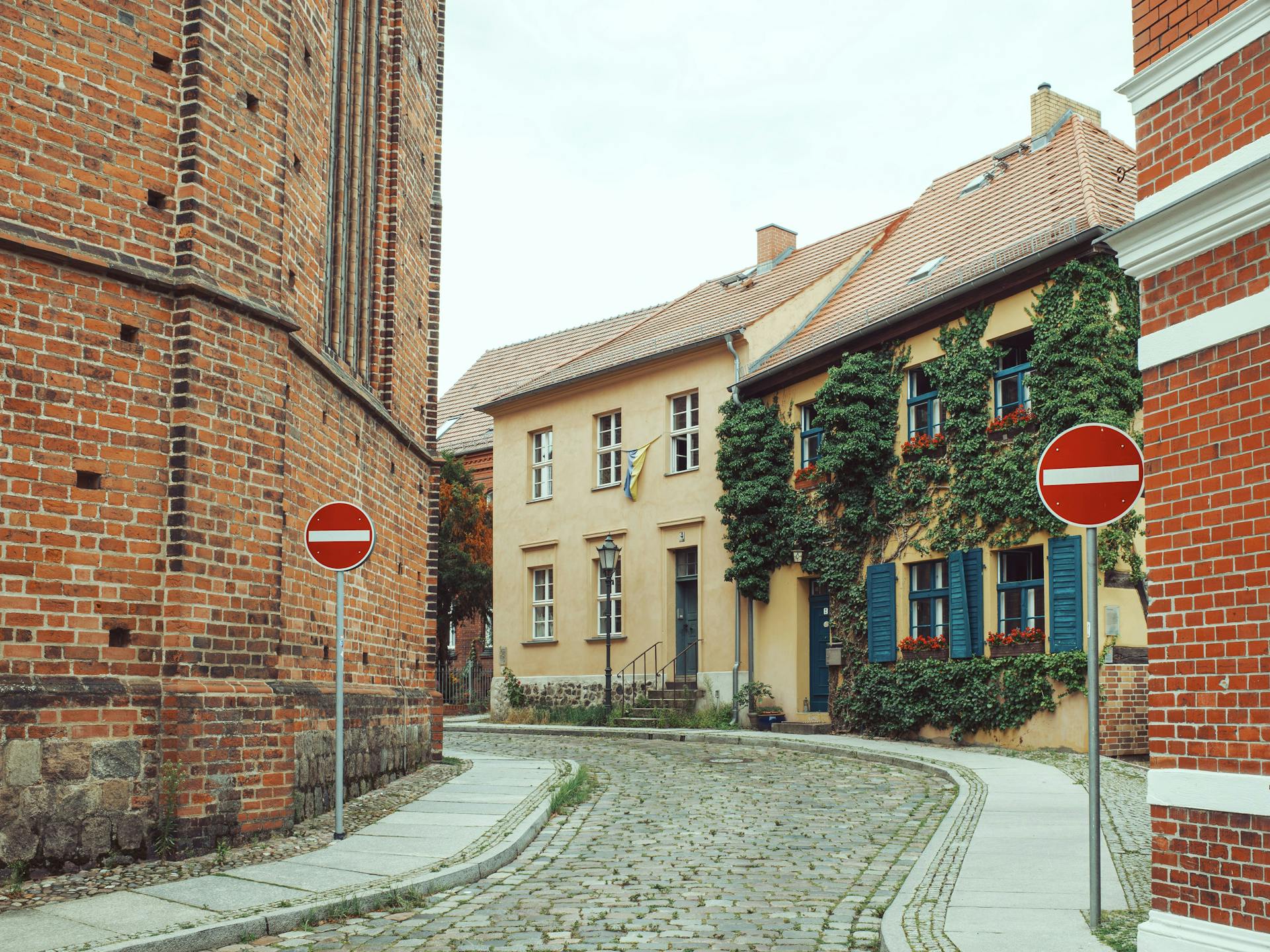 Cobblestone lane between a red-brick tower and an ivy-covered old townhouse in Bernau near Berlin.