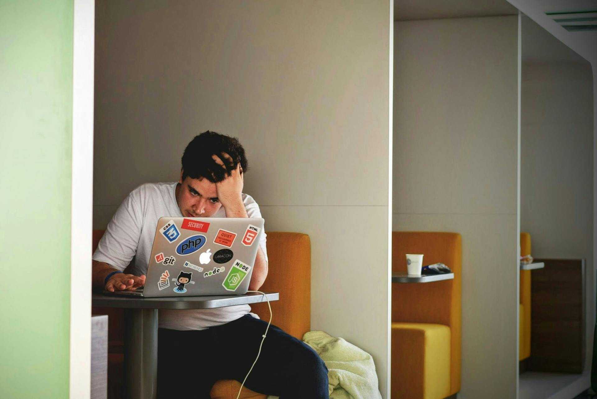 Gestresster Mann sitzt am Laptop und hält sich die Hand an den Kopf.