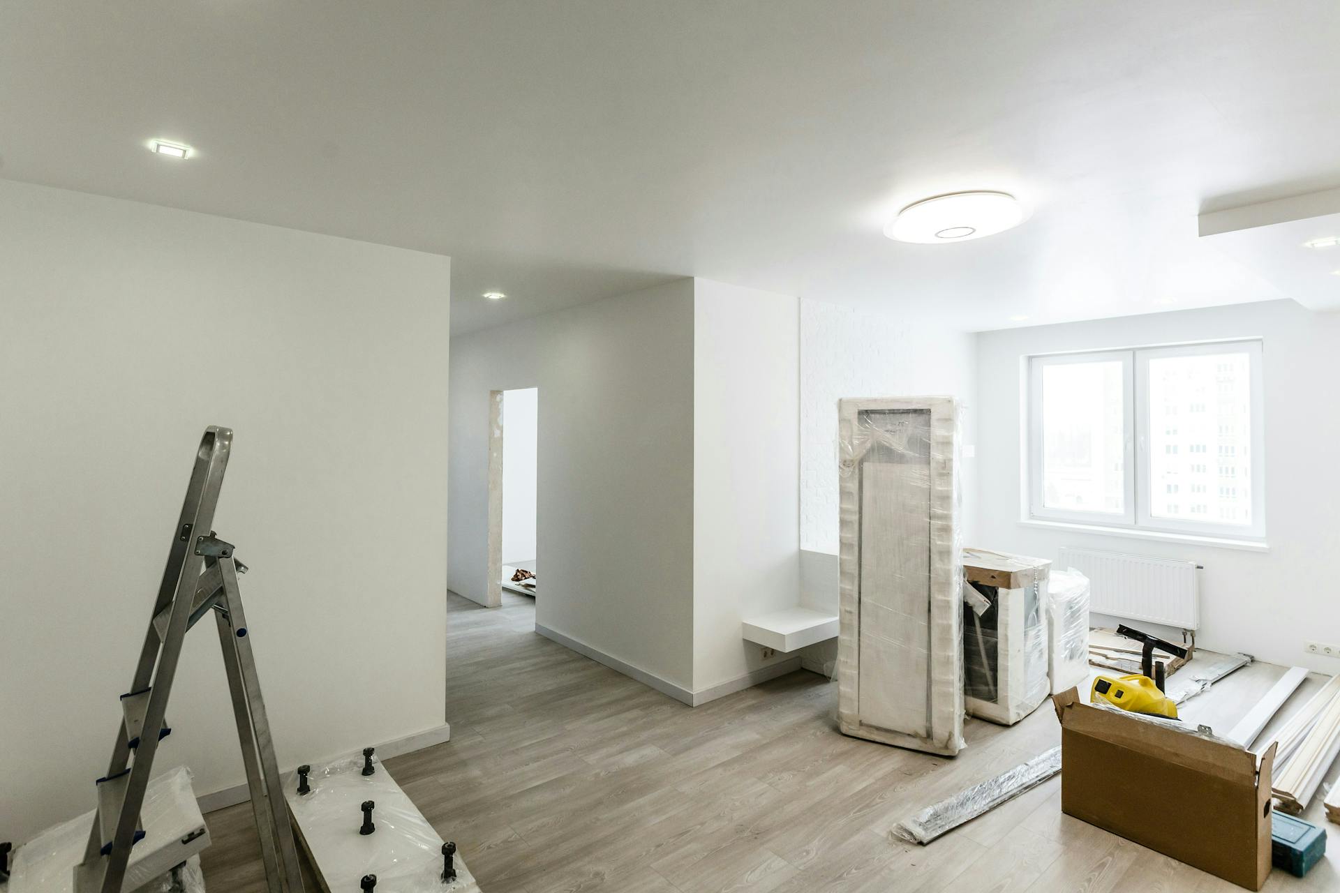 Room under renovation with a ladder, covered furniture, and moving boxes.