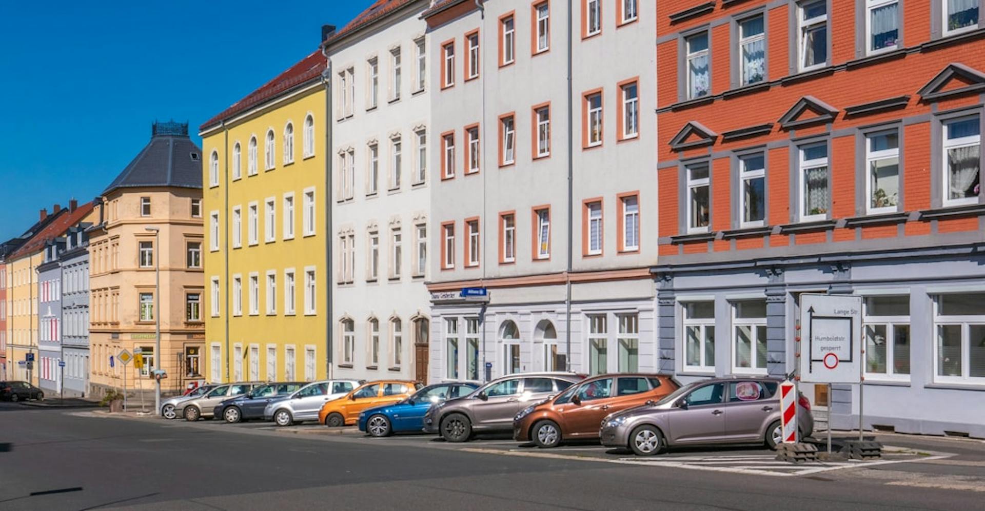 Bunte Altbaufassaden mit parkenden Autos entlang einer deutschen Straße.