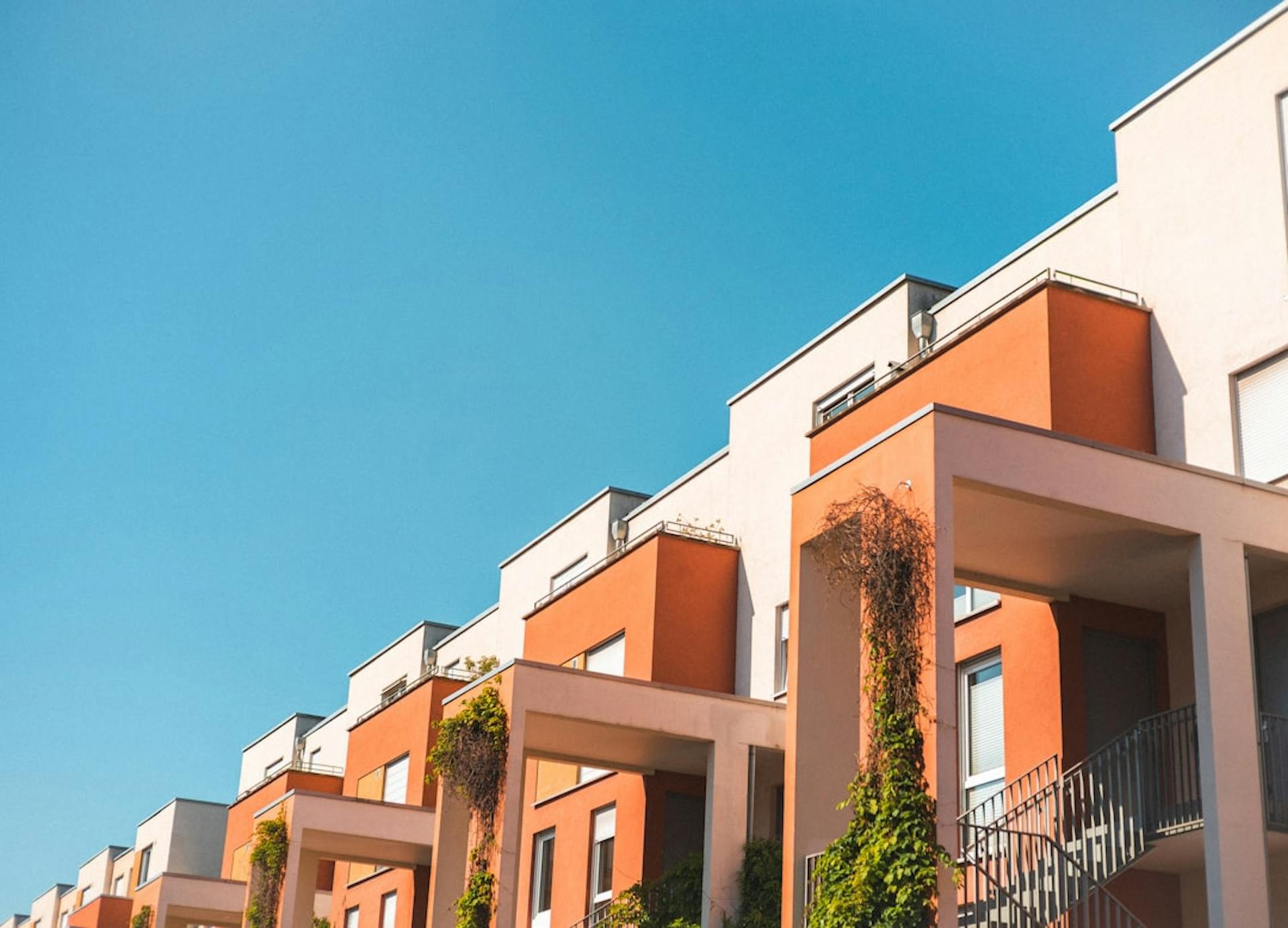 Row of modern apartment buildings with balconies and terraces under a blue sky.