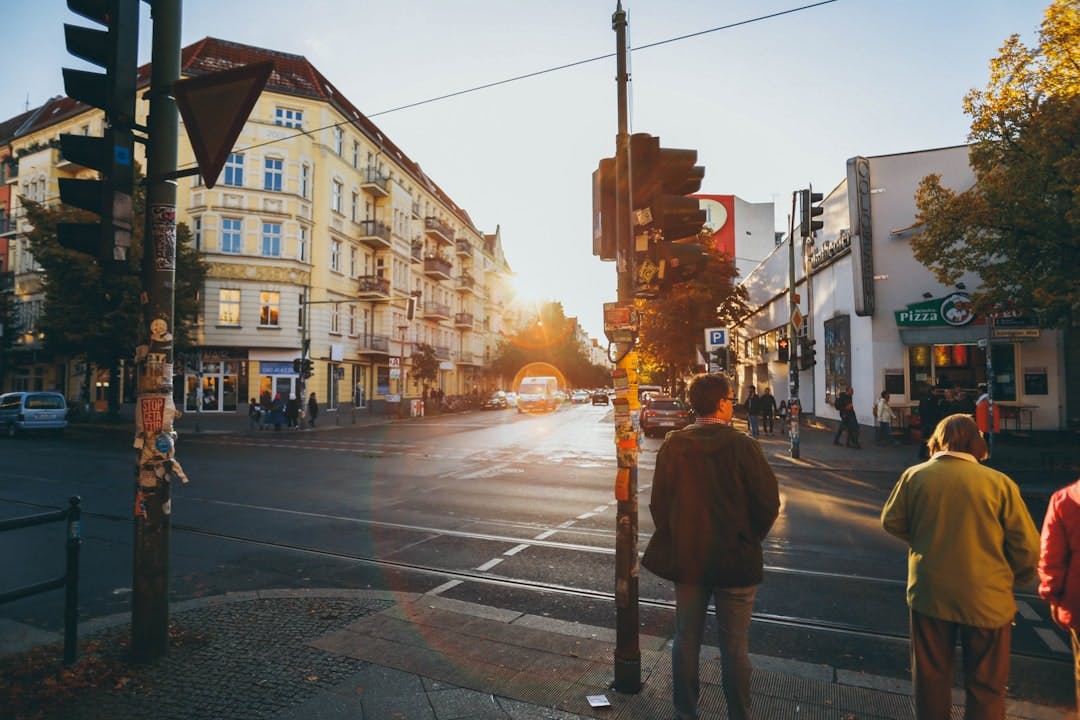 People waiting at a street crossing in Berlin at sunset, with yellow Altbau facades in the background.