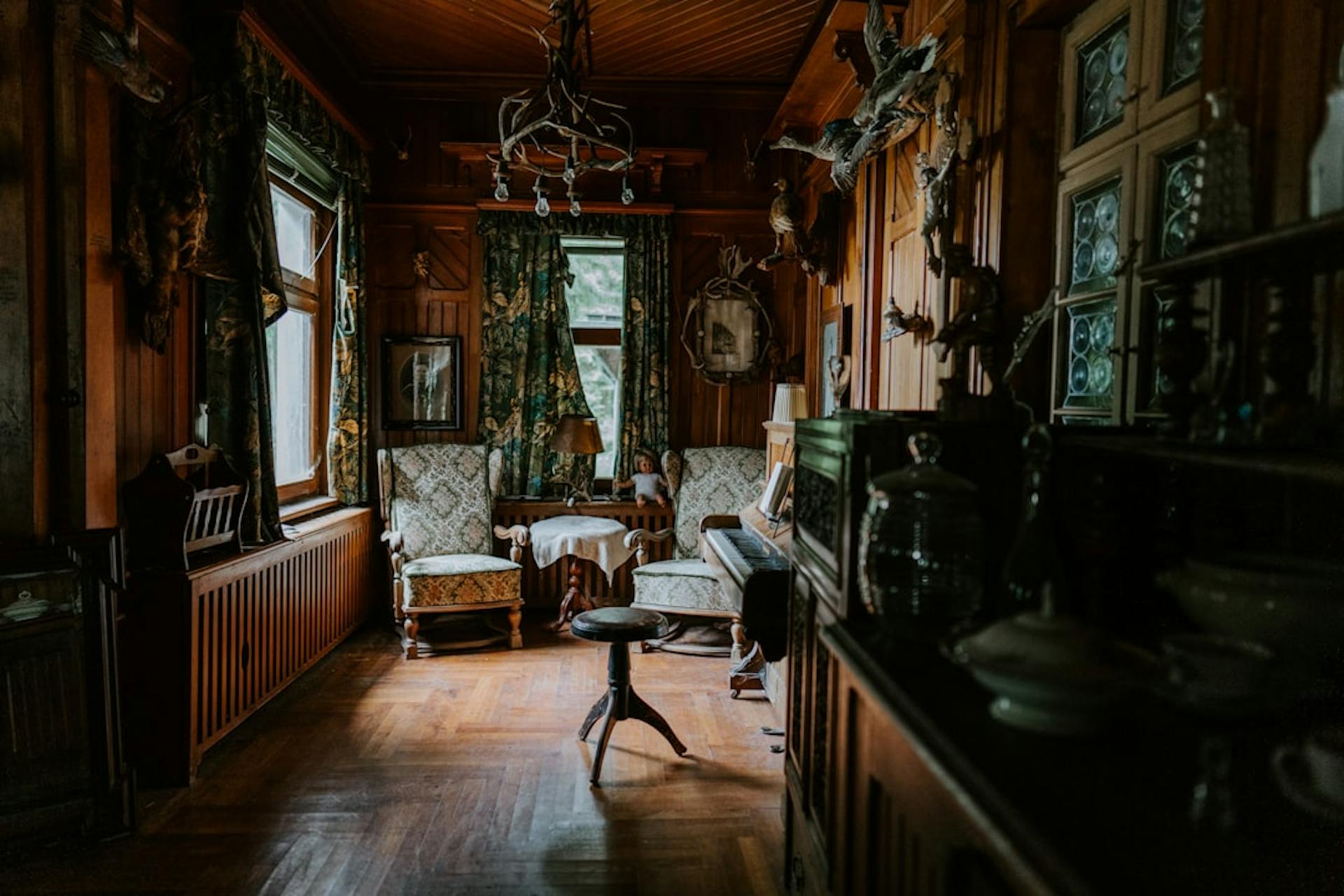 Rustic wood-paneled living room with antique furniture, patterned curtains and a parquet floor.