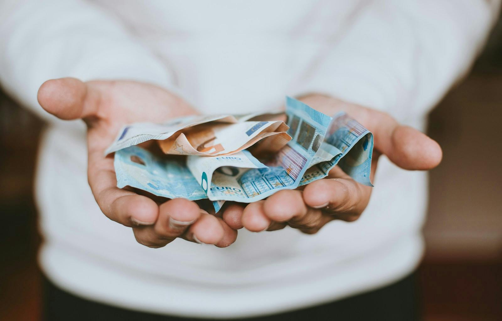 Person holding folded euro banknotes with both hands.