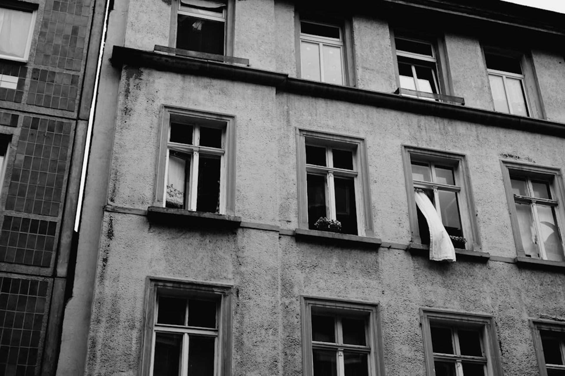 Black-and-white photo of a historic building facade with a curtain blowing out an open window.