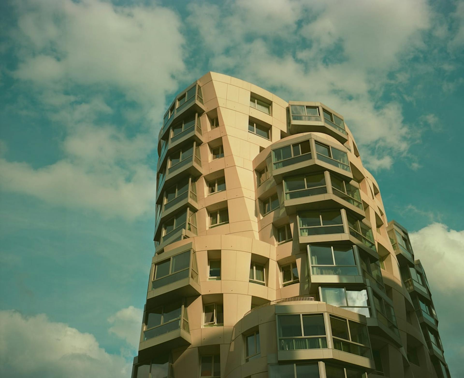 Modernes, geschwungenes Hochhaus mit Balkonen vor bewölktem Himmel.
