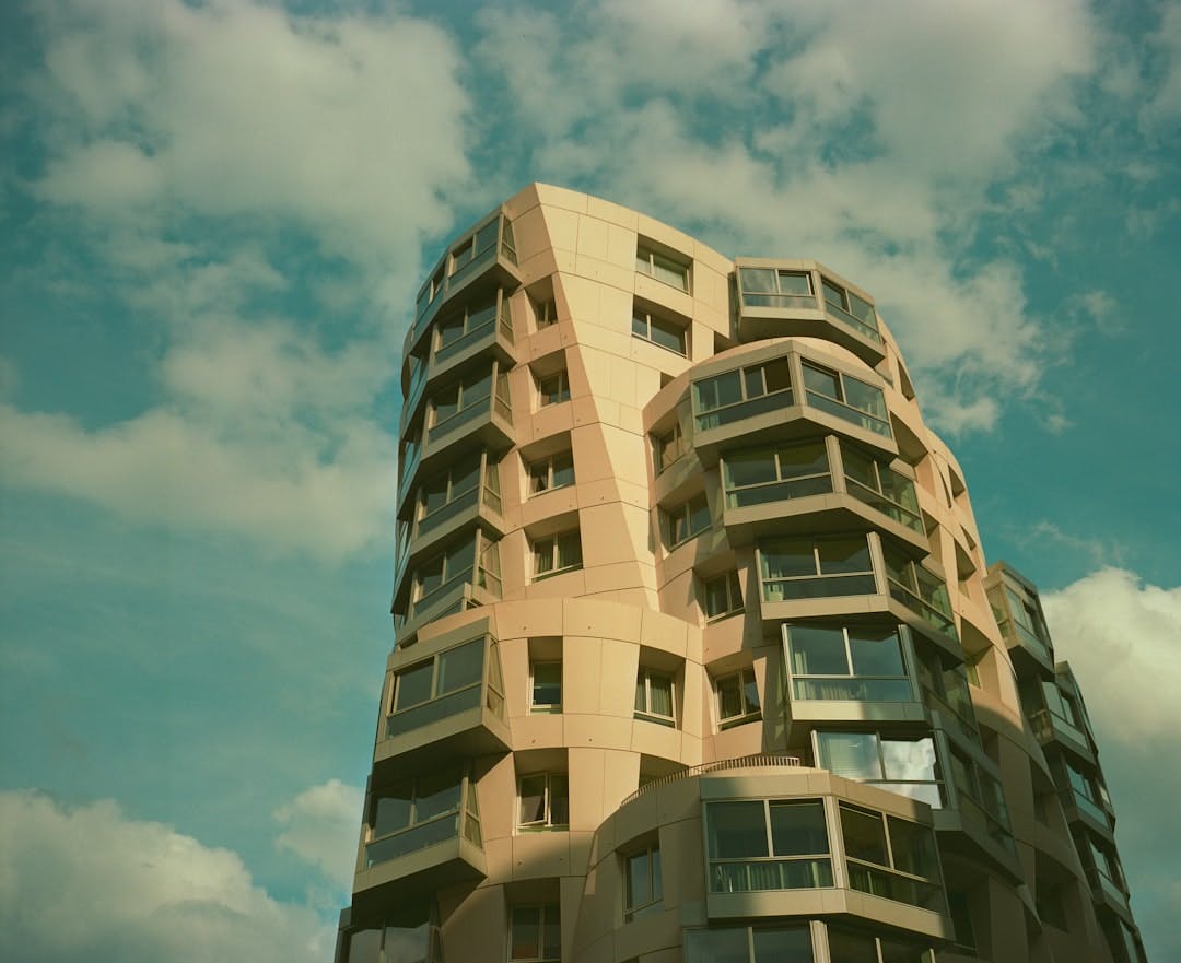 Modernes, geschwungenes Hochhaus mit Balkonen vor bewölktem Himmel.