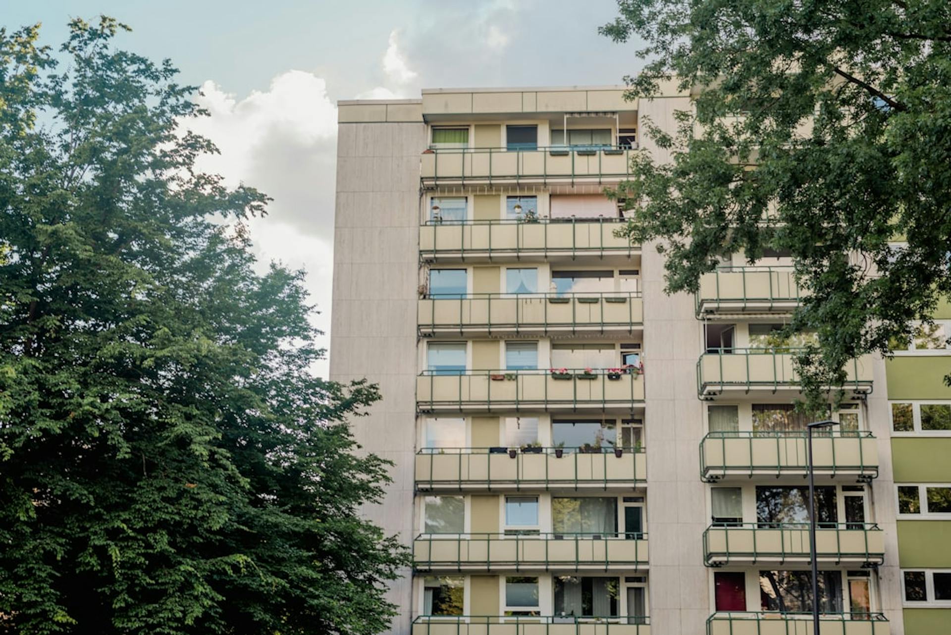 Multi-story high-rise apartment building with balconies behind trees.
