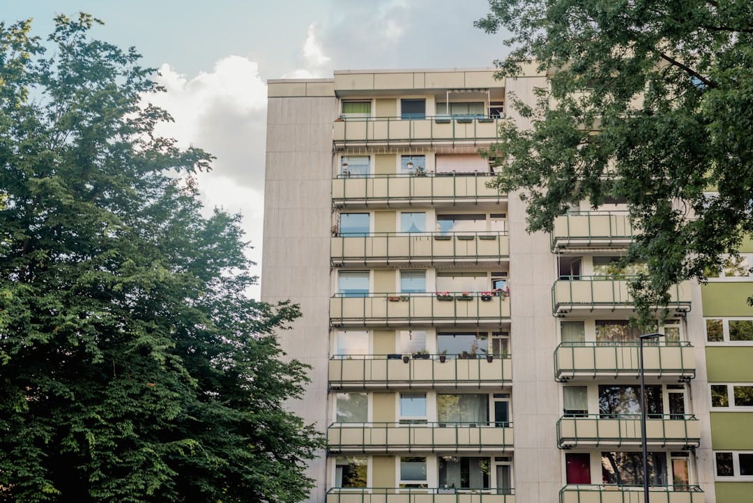 Multi-story high-rise apartment building with balconies behind trees.