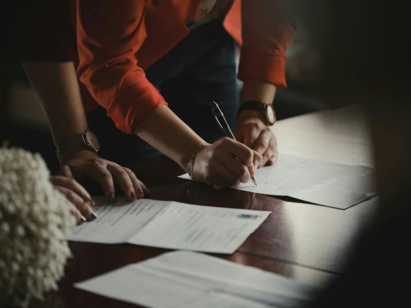Person signing a document about rent payments at a desk (Photo by Romain Dancre on Unsplash)