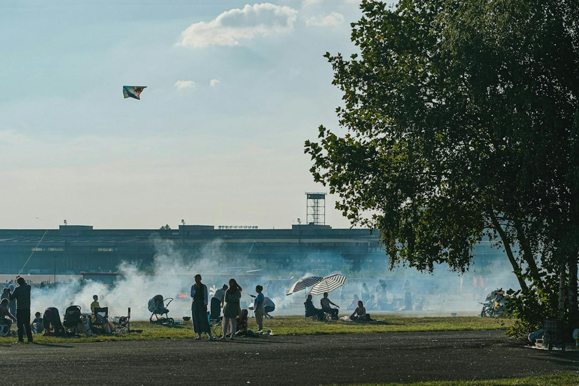 Gruppen grillen auf dem Tempelhofer Feld in Berlin, dahinter der alte Flughafen (Photo by Victoria Prymak on Unsplash)