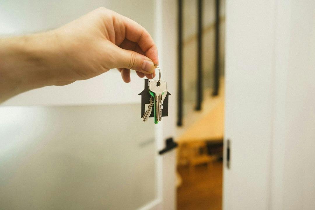 Hand holding a set of keys in front of an open apartment door (Photo by Jakub Żerdzicki on Unsplash)