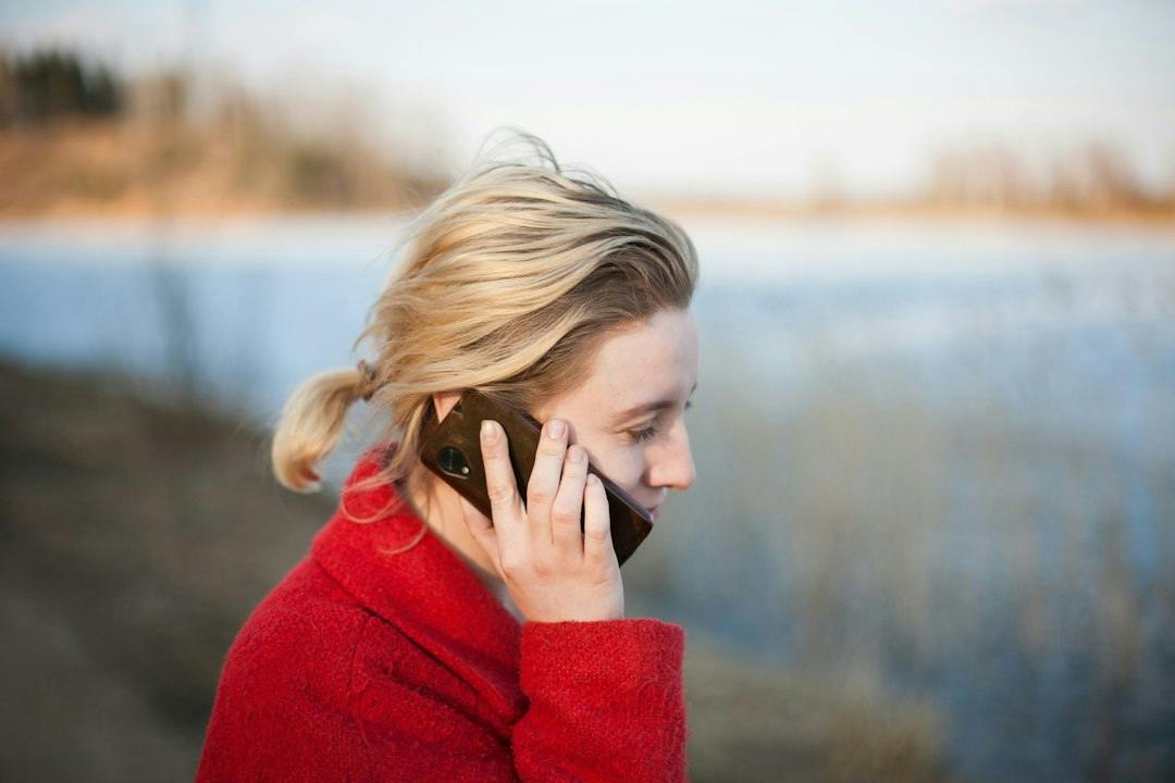 Young woman in a red sweater taking a phone call outdoors (Photo by Timur Repin on Unsplash)