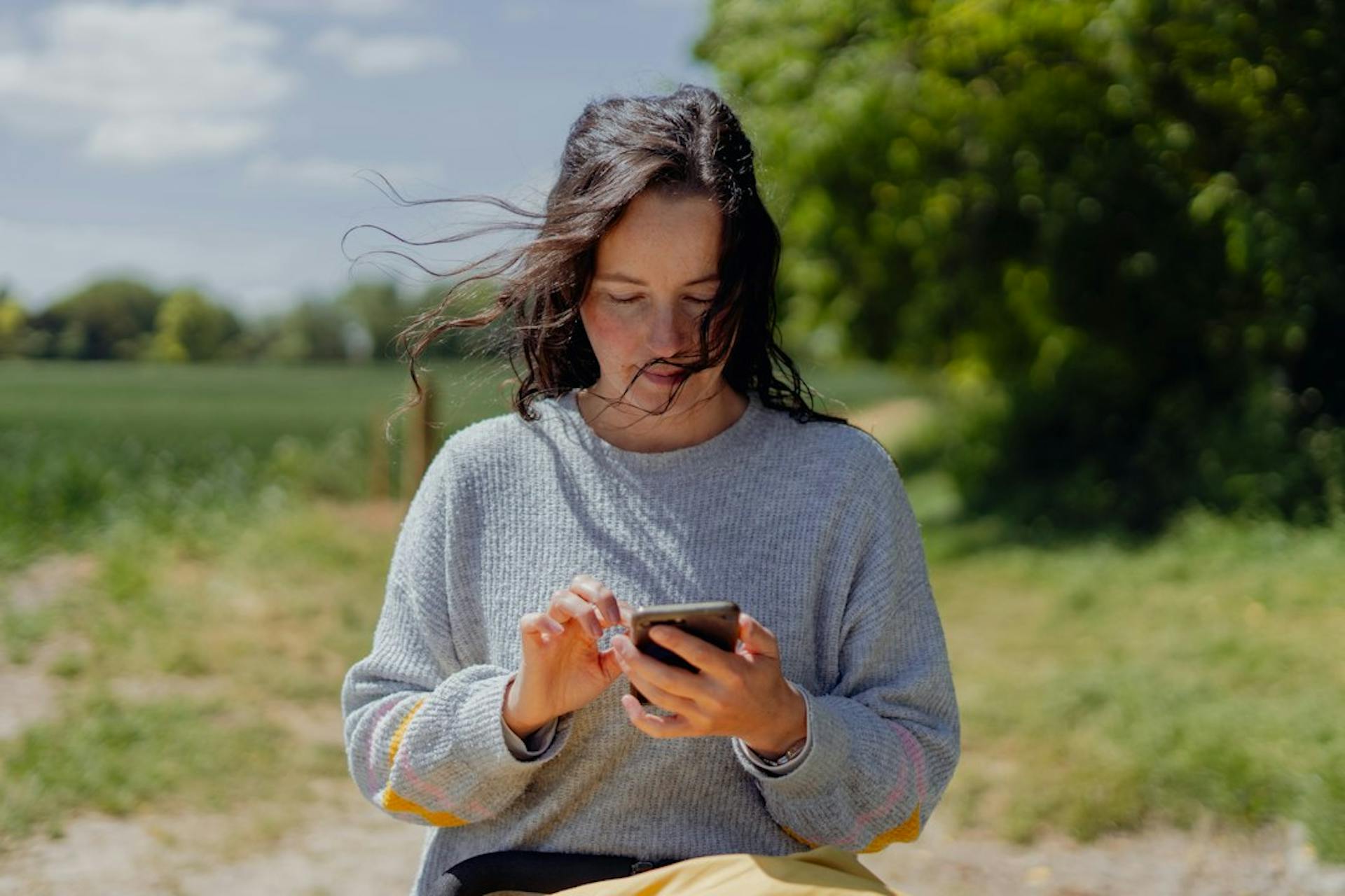 Young woman standing outdoors reading a message on her phone (Photo by BEN ELLIOTT on Unsplash)