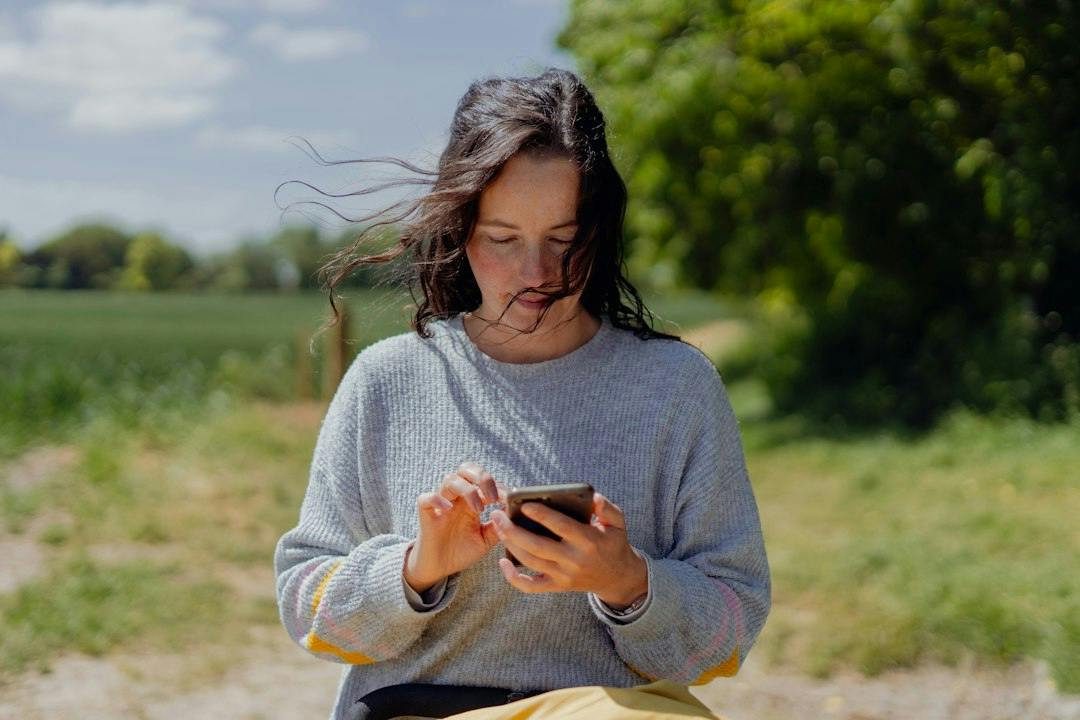 Young woman standing outdoors reading a message on her phone (Photo by BEN ELLIOTT on Unsplash)
