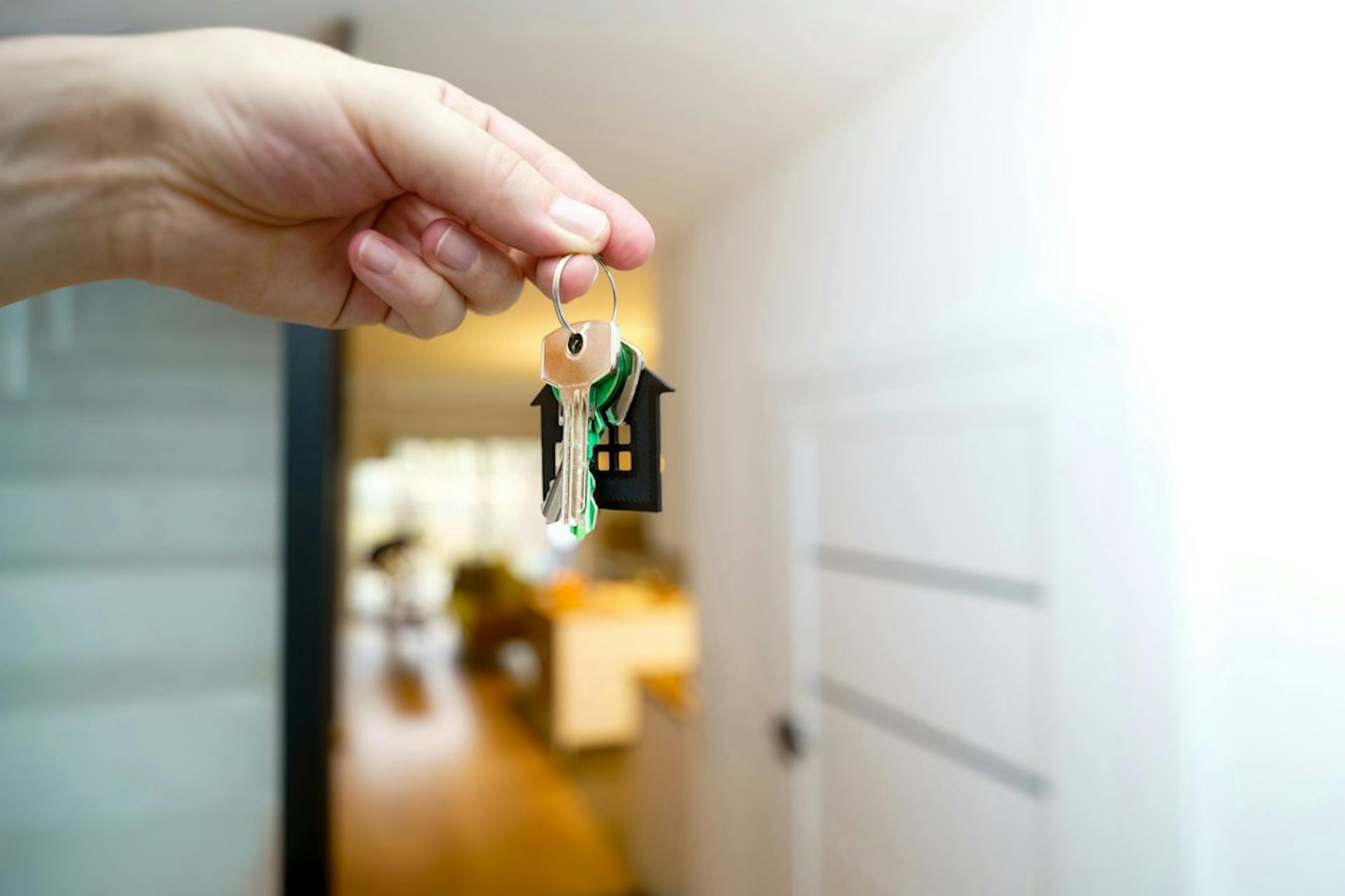 Hand holding house keys with a house-shaped keyring at an apartment entrance (Photo by Jakub Żerdzicki on Unsplash)
