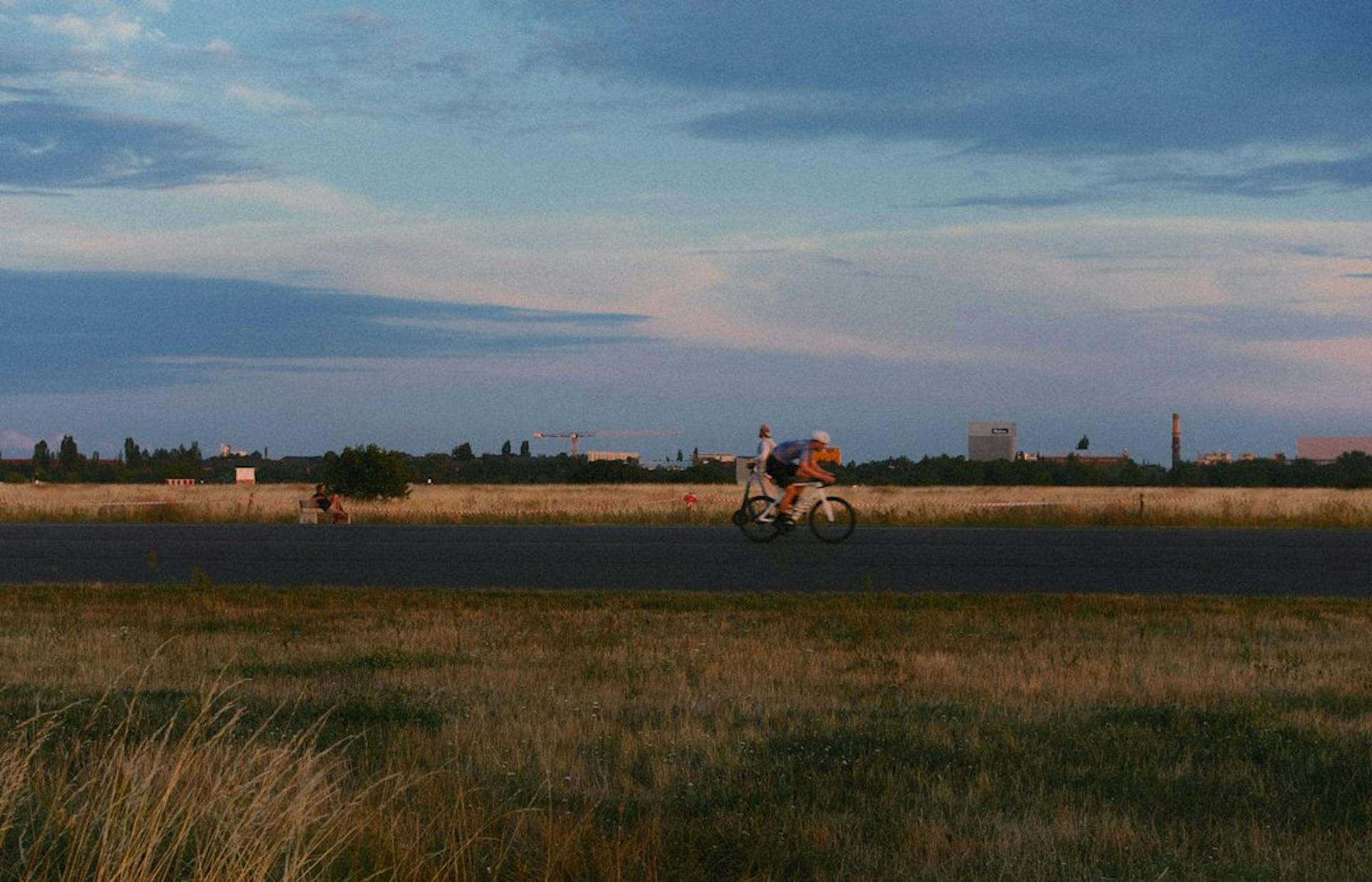 Young people cycling across a wide open field in Berlin (Photo by Amina on Unsplash)